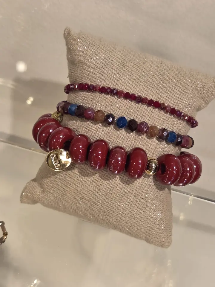 Drei Armbänder: große glänzende Perlen in Bordeaux mit goldfarbenem Anhänger, facettierte Perlen in Bordeaux sowie in Pflaume, Blau und Bernstein, Accessoires zur Herbstmode 2026 im Mode-Atelier Völkl, Haar bei München