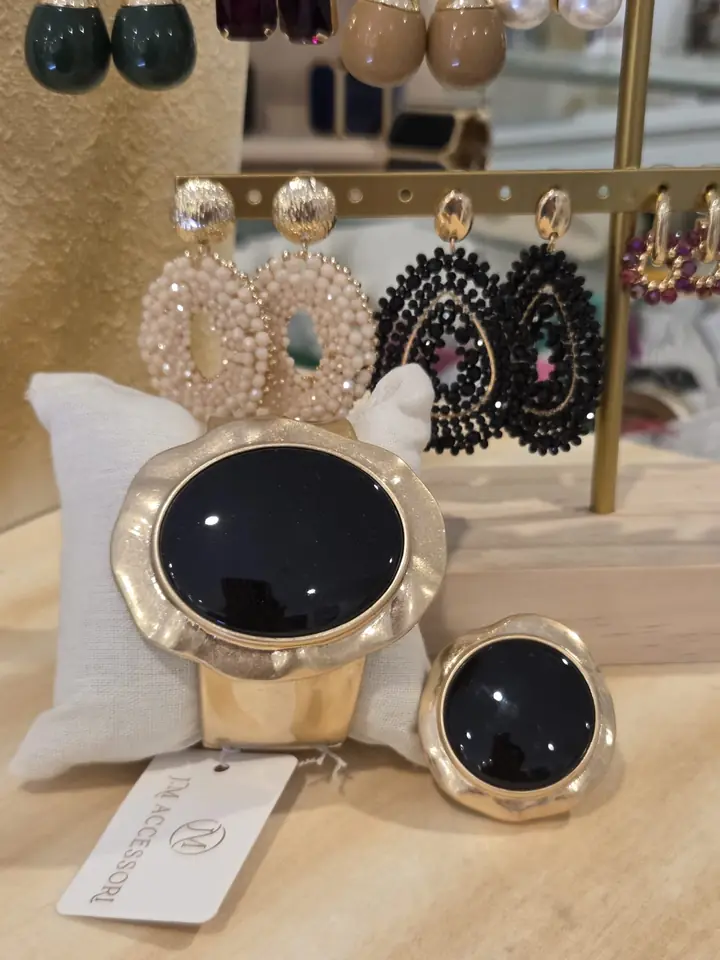 Breiter Armreif in mattem Champagner-Gold mit großem schwarzem Cabochon und passender Ring, dahinter Perlen-Ohrringe in Creme und Schwarz, Accessoires zur Herbstmode 2026 im Mode-Atelier Völkl, Haar bei München
