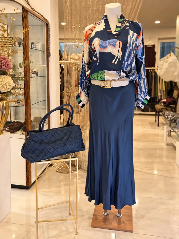 Bluse mit Pferde-Print in Blau, Weiß, Orange und Grün zu fließendem Maxirock in Satin-Optik in Marine, weißer Gürtel mit goldfarbener Schnalle und geflochtene Henkeltasche in Marine, Herbstmode 2026 im Mode-Atelier Völkl, Haar bei München