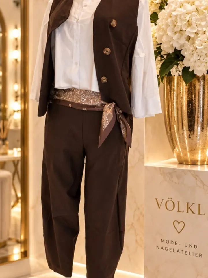Weste mit großen Knöpfen und Hose in Schokobraun über weißer Bluse mit weiten Ärmeln, gemustertes Tuch als Gürtel, Herbstmode 2026 im Mode-Atelier Völkl, Haar bei München